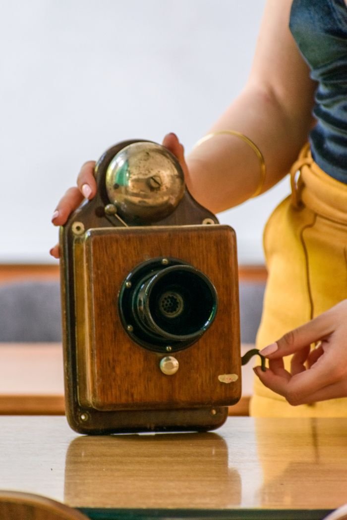 Close-up view of a hand-held vintage wooden wall telephone with a bell.